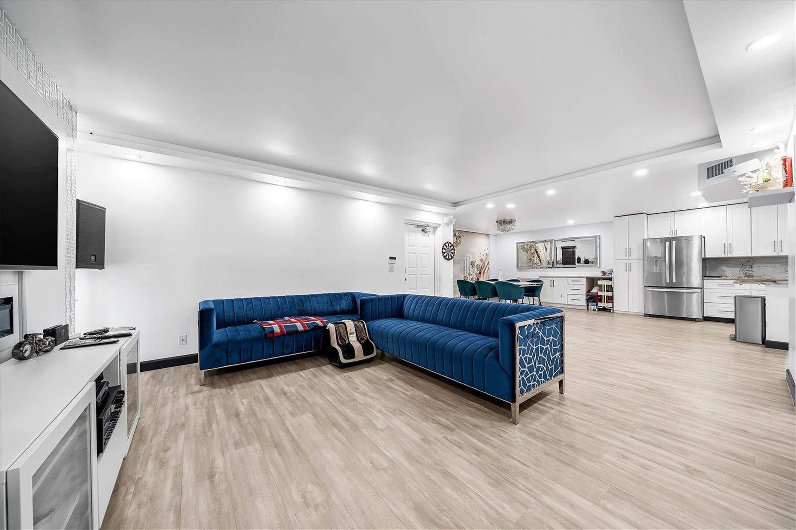 A modern open-concept living room features a blue velvet sectional sofa and a white kitchen — 13790 Oneida Drive # B1, Delray Beach FL 33446, DELRAY BEACH, FL