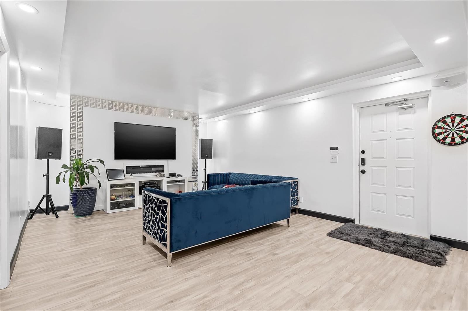 A living room features a blue velvet sofa, a wall-mounted television, and a dartboard — 13790 Oneida Drive # B1, Delray Beach FL 33446, DELRAY BEACH, FL