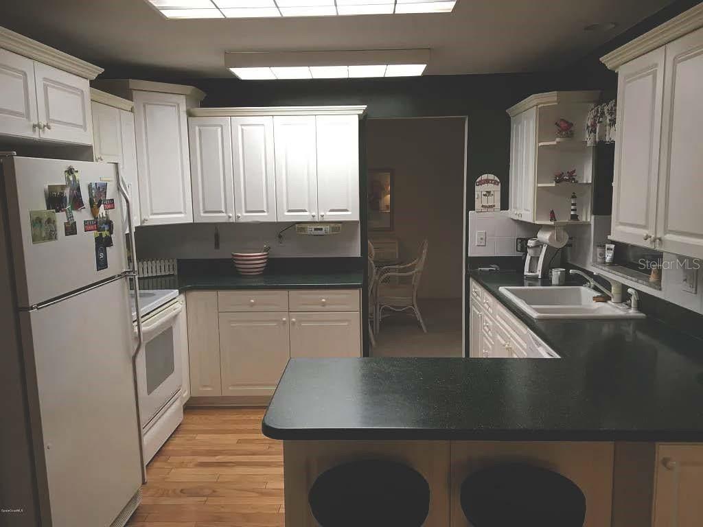 A kitchen with white cabinets, black countertops, a white refrigerator, and wood flooring — 4825 SQUIRES DRIVE, TITUSVILLE, FL