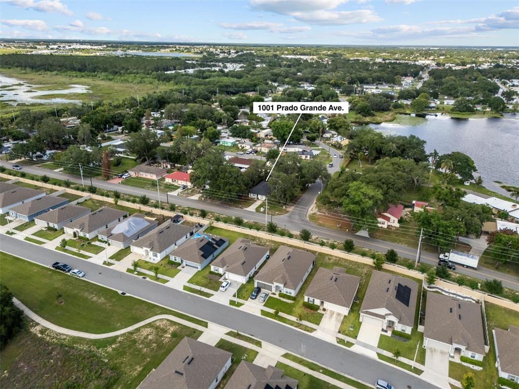An aerial view shows a suburban neighborhood with houses, a lake, and a road — 1001 PRADO GRANDE AVENUE, HAINES CITY, FL