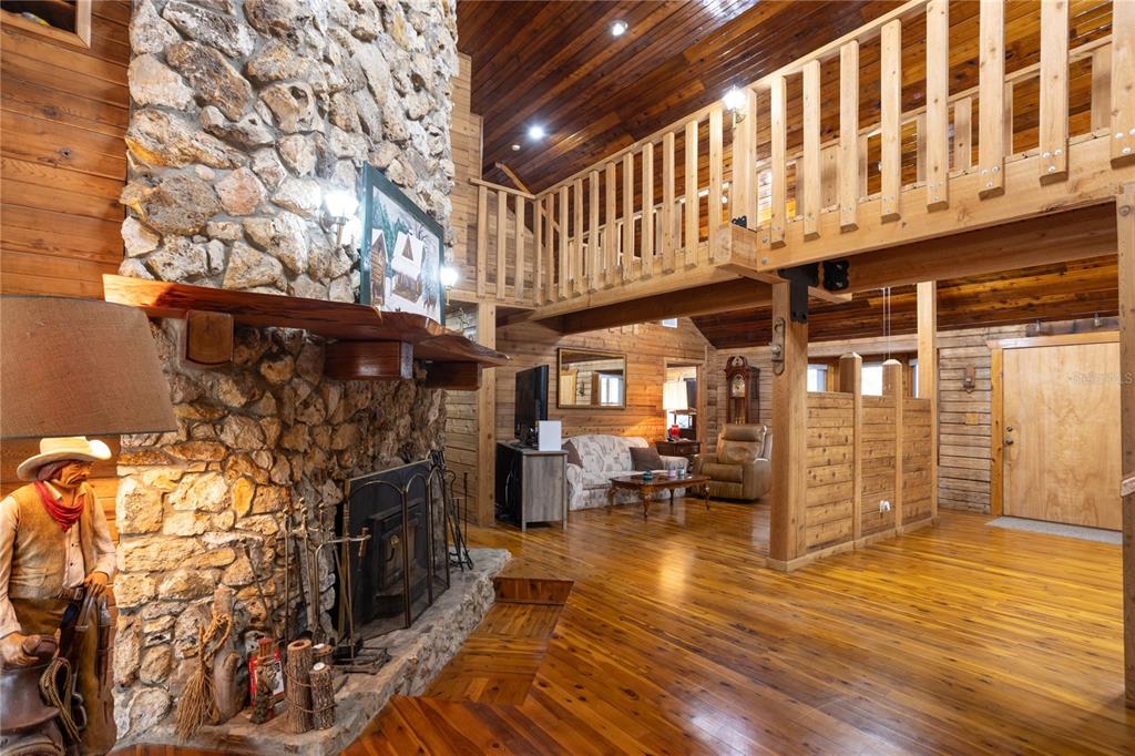 A rustic living room features wood-paneled walls, a stone fireplace, and a lofted balcony — 6892 SWAIN ROAD, SORRENTO, FL