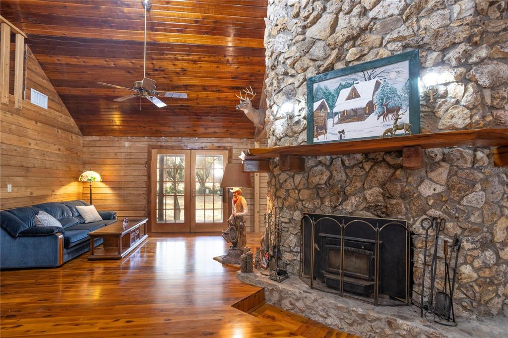 A rustic living room features a large stone fireplace, wood-paneled walls, and a wooden loft railing — 6892 SWAIN ROAD, SORRENTO, FL