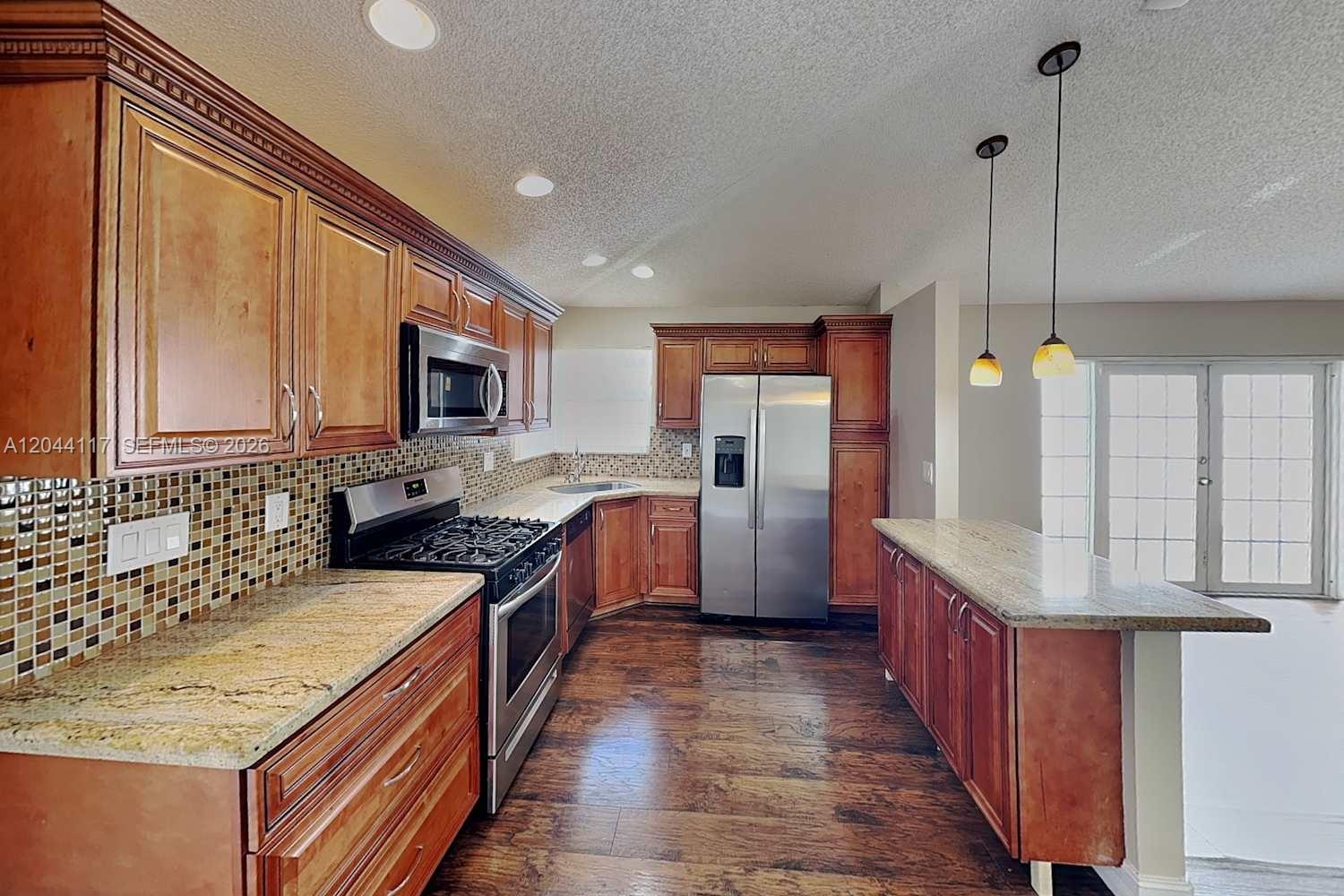 A kitchen features wood cabinets, granite countertops, stainless steel appliances, and a tile backsplash — PLANTATION, FL