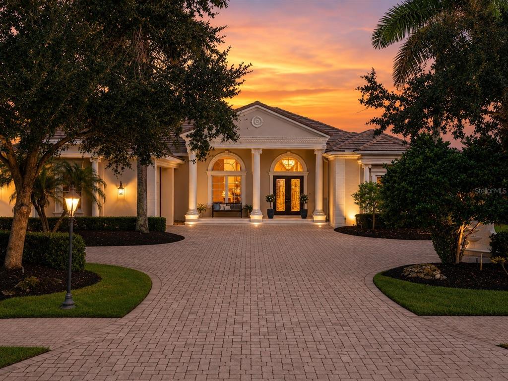A paved driveway leads to the front entrance of a house with white columns at sunset — 3360 FOUNDERS CLUB DRIVE, SARASOTA, FL
