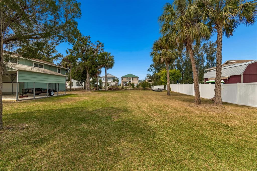 A large, grassy backyard features palm trees, a white vinyl fence, and neighboring houses — 14539 COFFEY LANE, HUDSON, FL