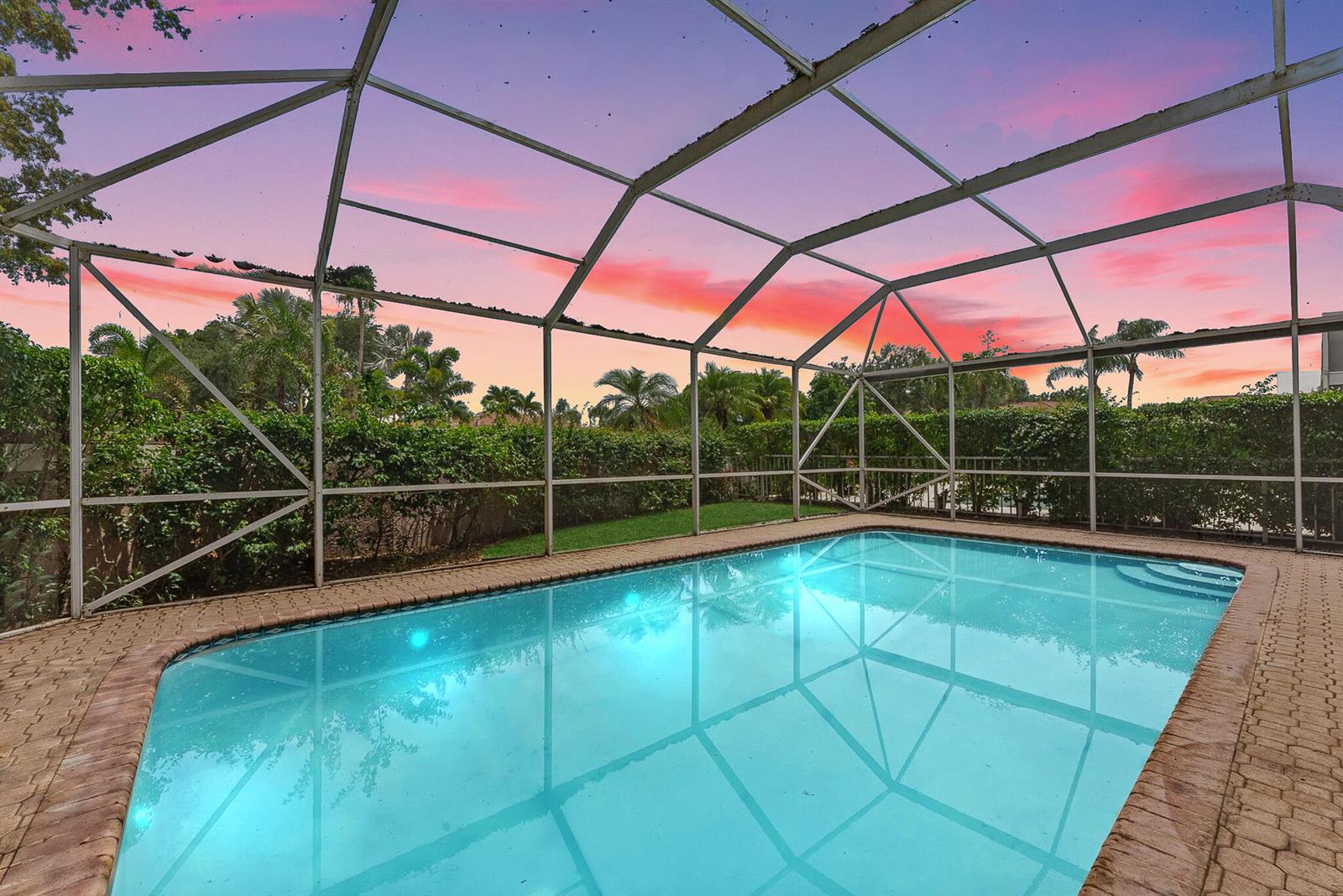A swimming pool is enclosed by a screened lanai with a sunset view in the background — 3938 Redondo Court, Boca Raton FL 33487, BOCA RATON, FL