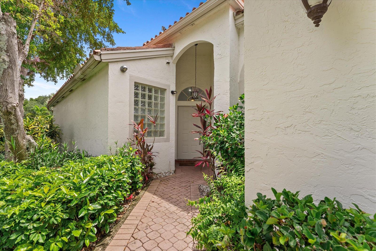 A paved walkway leads to the front entrance of a white stucco house with glass blocks — 3938 Redondo Court, Boca Raton FL 33487, BOCA RATON, FL