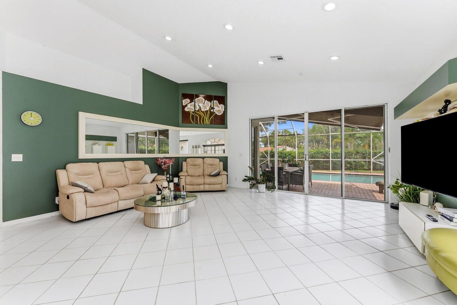 A living room with green walls, white tile floors, and sliding doors overlooking a pool — 3938 Redondo Court, Boca Raton FL 33487, BOCA RATON, FL