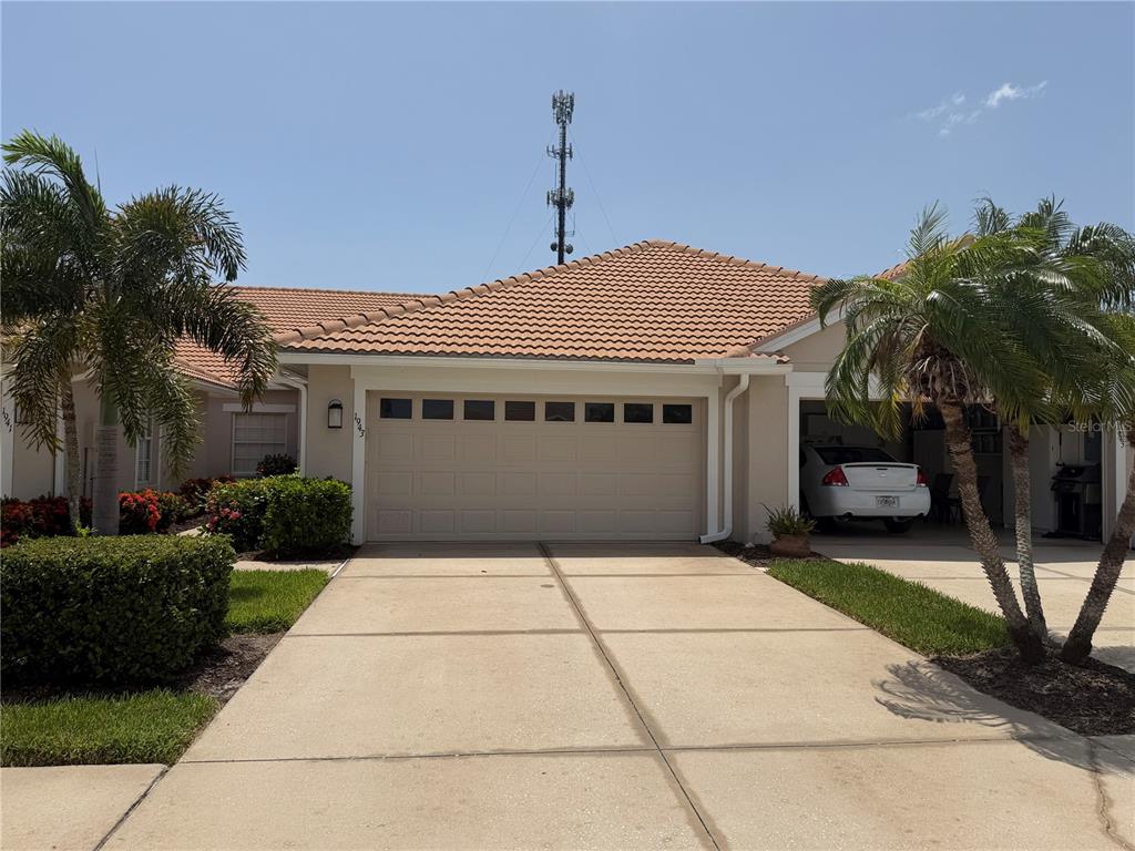 A beige house with a tiled roof, a two-car garage, and palm trees in front — 1943 SAN SILVESTRO DRIVE, VENICE, FL