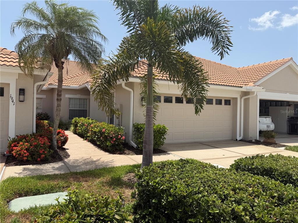 A beige house exterior features a two-car garage, palm trees, and a landscaped walkway — 1943 SAN SILVESTRO DRIVE, VENICE, FL