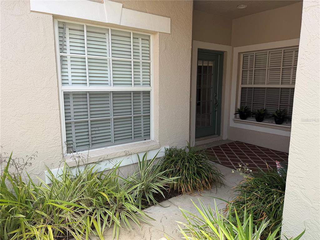 A view of a home entrance with a front door, windows with shutters, and landscaping — 1943 SAN SILVESTRO DRIVE, VENICE, FL
