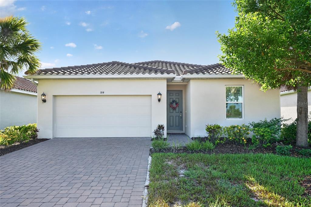 A single-story house with a beige stucco exterior, a two-car garage, and a paved driveway — 184 DAYLILY BOULEVARD, NOKOMIS, FL