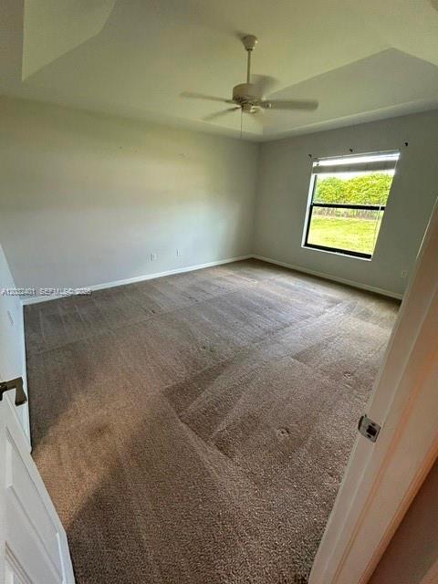 An empty bedroom with beige carpeting, a tray ceiling with a fan, and a window — 20 NE 20th Ave, Cape Coral FL 33909, CAPE CORAL, FL