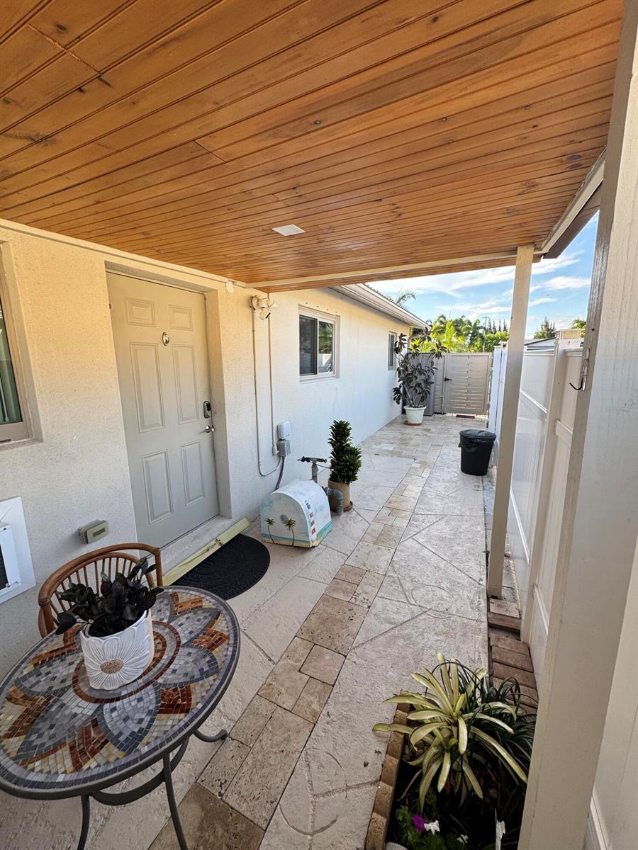 A covered patio features a mosaic table, a light-colored door, and stone-patterned tile flooring — 2664 Exuma Road, West Palm Beach FL 33406, WEST PALM BEACH, FL