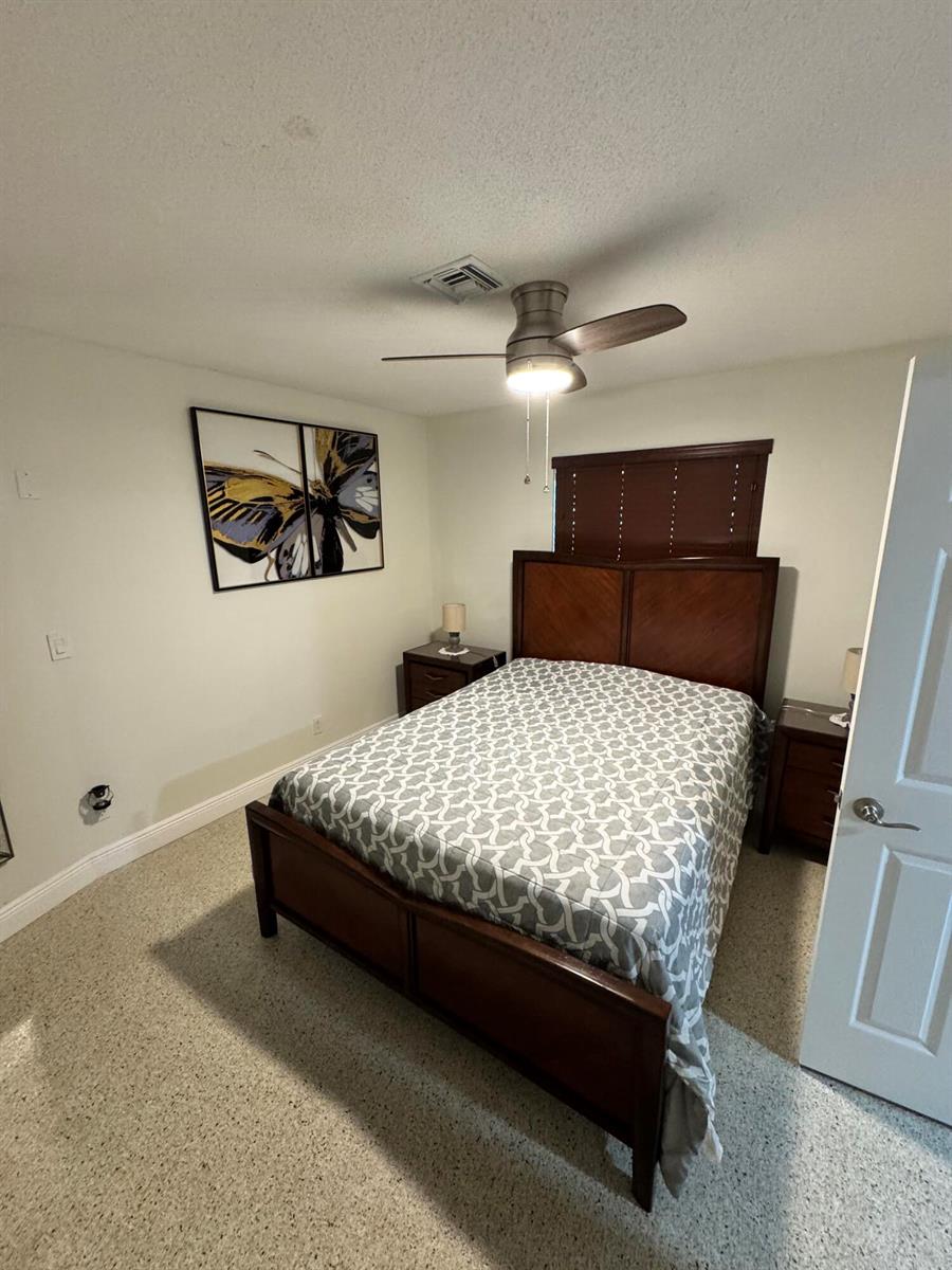 A bedroom features a wooden bed frame, patterned bedding, two nightstands, and a ceiling fan — 2664 Exuma Road, West Palm Beach FL 33406, WEST PALM BEACH, FL
