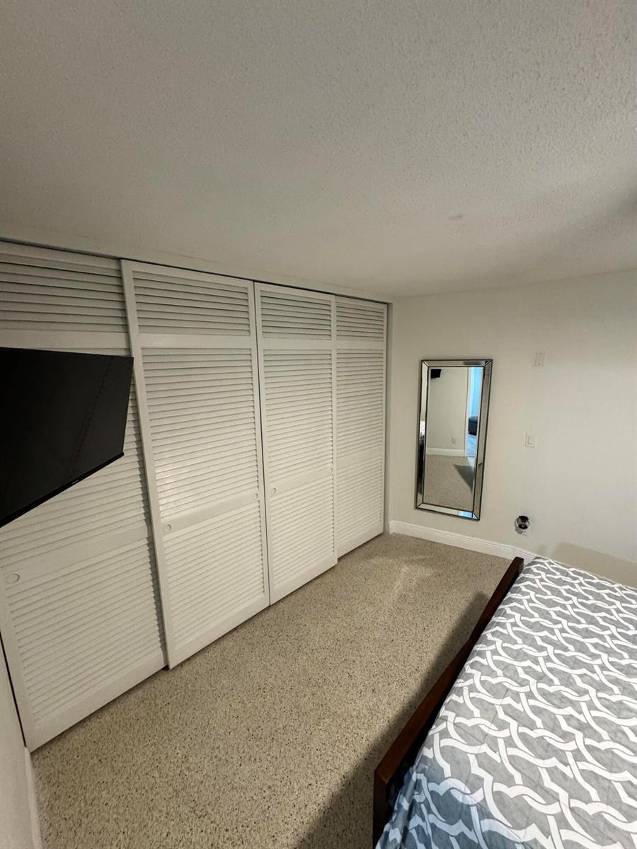 A bedroom features white louvered closet doors, a wall-mounted television, and a full-length mirror — 2664 Exuma Road, West Palm Beach FL 33406, WEST PALM BEACH, FL