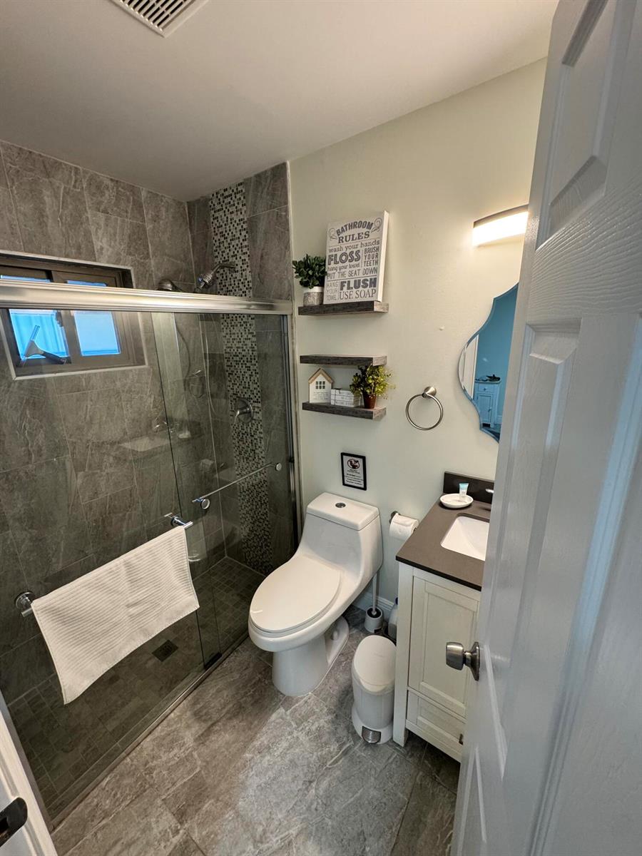 A small bathroom features a glass-enclosed shower, a white toilet, and a vanity with a mirror — 2664 Exuma Road, West Palm Beach FL 33406, WEST PALM BEACH, FL