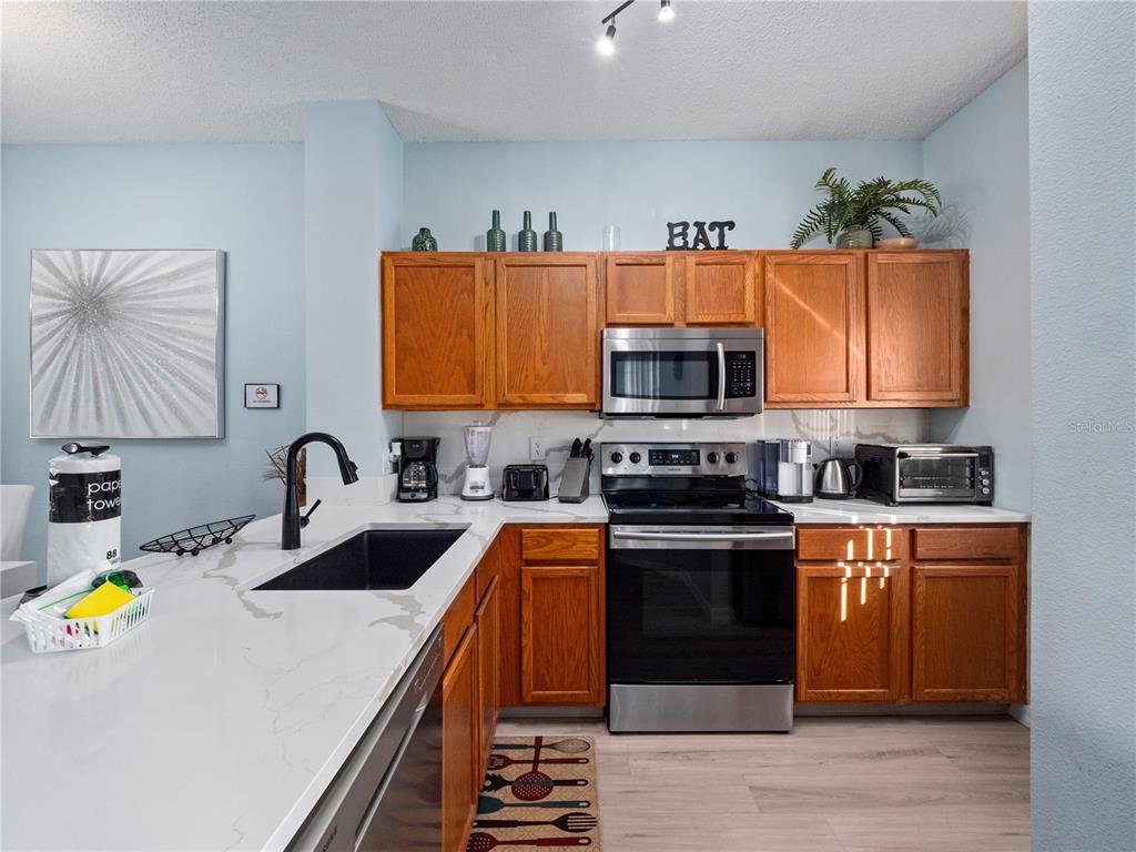 A kitchen features wood cabinets, stainless steel appliances, and white countertops with gray veining — 136 POMPANO BEACH DRIVE, KISSIMMEE, FL