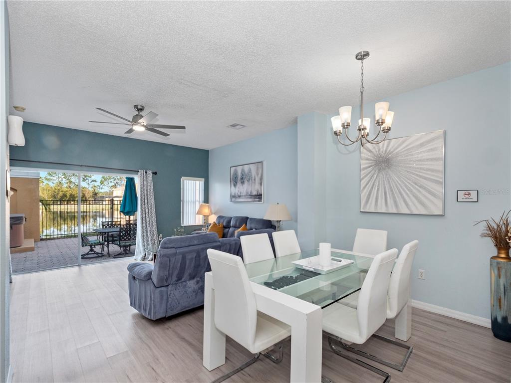 A dining area with a glass table and chairs sits beside a living room with lake views — 136 POMPANO BEACH DRIVE, KISSIMMEE, FL