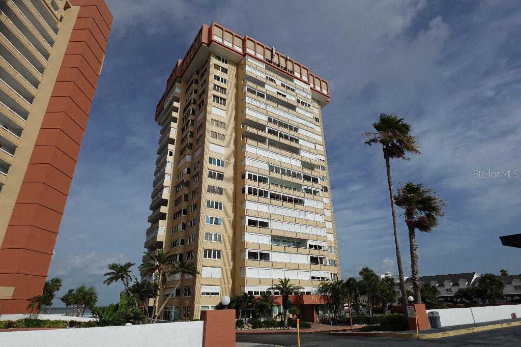 A tall, multi-story residential building with balconies stands under a blue sky with palm trees — 17920 GULF BOULEVARD UNIT 803, REDINGTON SHORES, FL