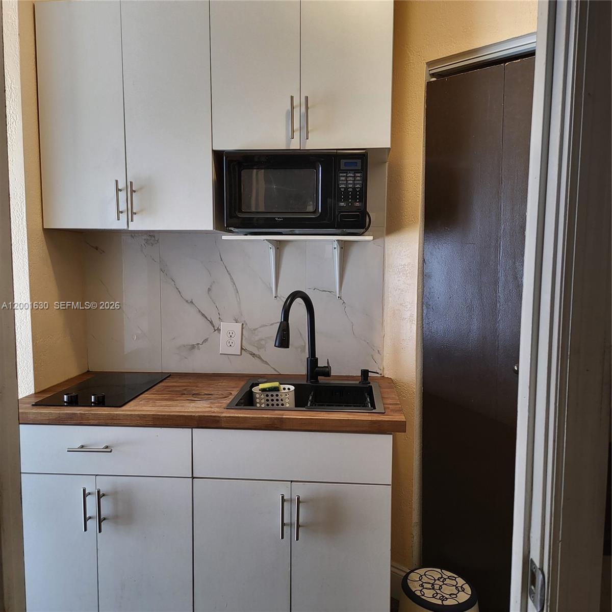 A small kitchen features white cabinets, a wood countertop, a black sink, and a microwave — 315 NW 59th St # 1, Miami FL 33127, MIAMI, FL
