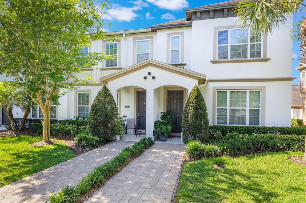 A two-story townhouse exterior features white stucco walls, dark doors, and a paved walkway — 11933 WATER RUN ALLEY, WINDERMERE, FL