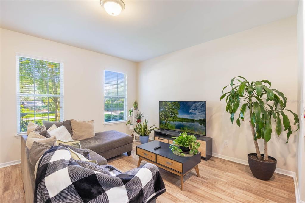 A living room features a gray sectional sofa, a television on a console, and a large plant — 11933 WATER RUN ALLEY, WINDERMERE, FL