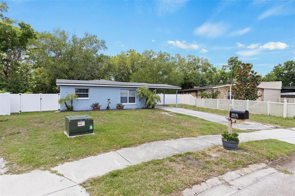A light blue single-story house with a carport and white vinyl fencing in the yard — 5508 WHITMORE DRIVE, TAMPA, FL