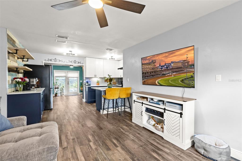 A living room with wood-look flooring, a white media console, and an open-concept kitchen — 5508 WHITMORE DRIVE, TAMPA, FL