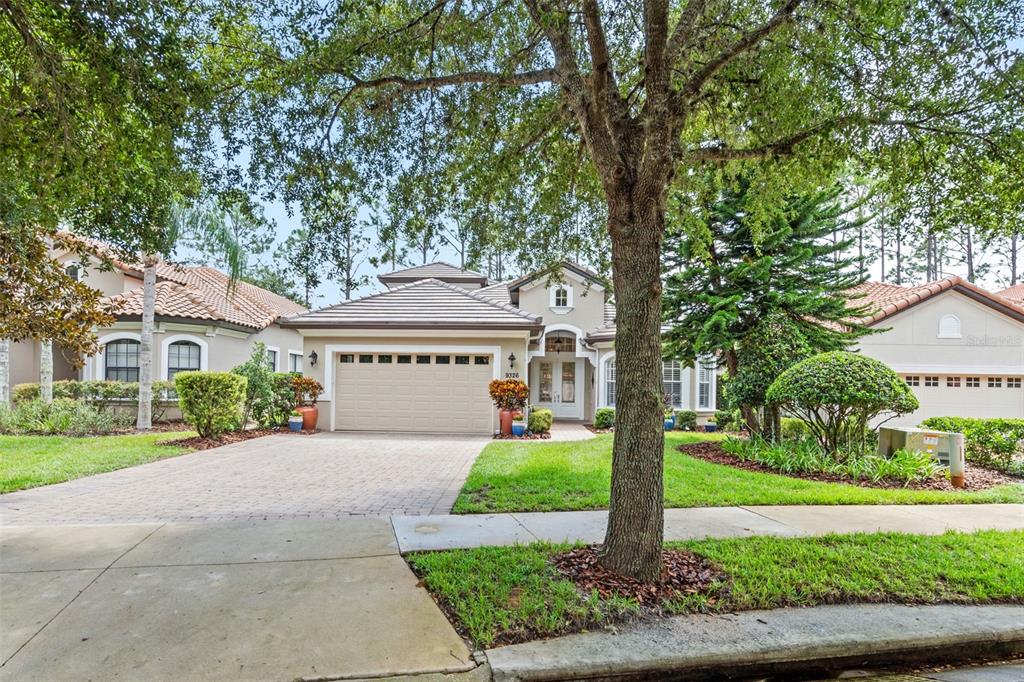 A single-story suburban house with a paved driveway, two-car garage, and a large front tree — 9326 SAN JOSE BLVD, HOWEY IN THE HILLS, FL