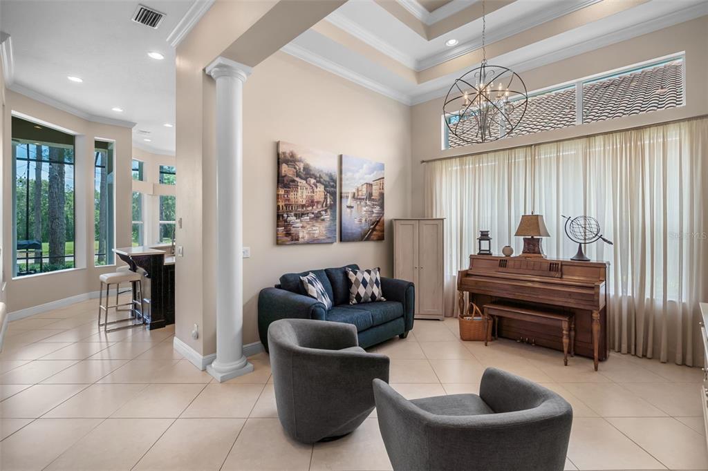 A living room features a piano, a dark blue sofa, two armchairs, and tile flooring — 9326 SAN JOSE BLVD, HOWEY IN THE HILLS, FL