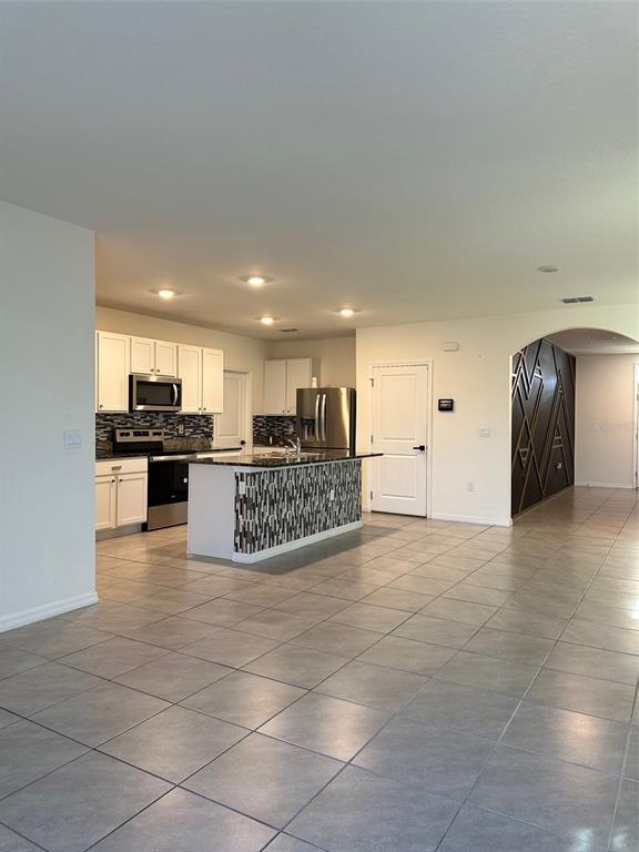 A kitchen with white cabinets, a tiled island, and stainless steel appliances opens to a hallway — 5703 HOLLINGWORTH TRAIL, WESLEY CHAPEL, FL