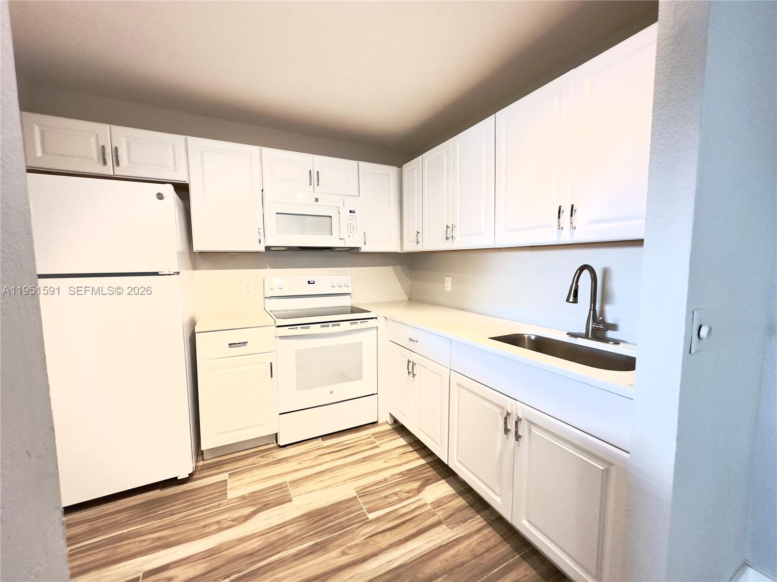 A kitchen features white cabinets, white appliances, a stainless steel sink, and wood-look flooring — 58 Monaco B # 58, Delray Beach FL 33446, DELRAY BEACH, FL