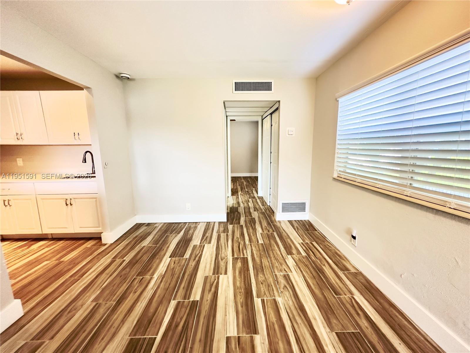 A room with wood-look tile flooring, a window with blinds, and an adjacent kitchen area — 58 Monaco B # 58, Delray Beach FL 33446, DELRAY BEACH, FL