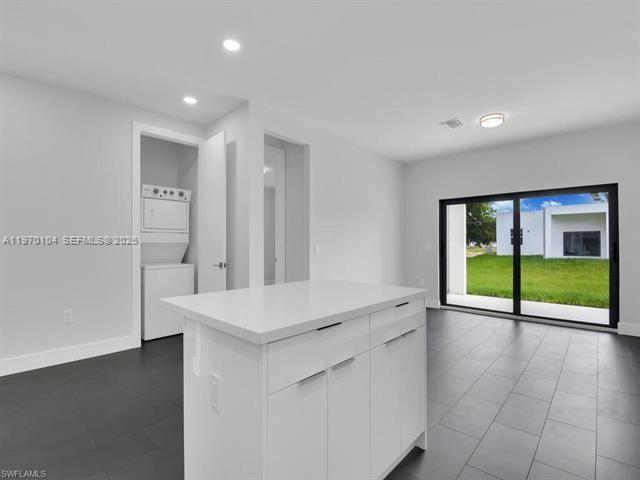 A modern kitchen area features a white island, dark tile floors, and a laundry closet — 834/836 Motel St E, Lehigh Acres FL 33974, LEHIGH ACRES, FL