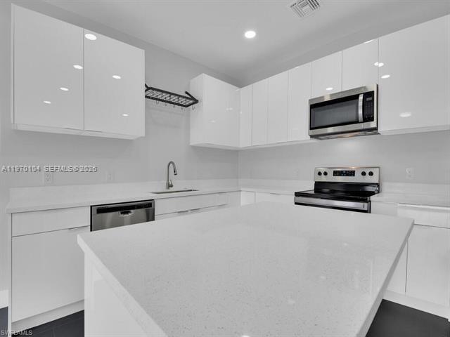 A modern kitchen features white high-gloss cabinets, a quartz island, and stainless steel appliances — 834/836 Motel St E, Lehigh Acres FL 33974, LEHIGH ACRES, FL