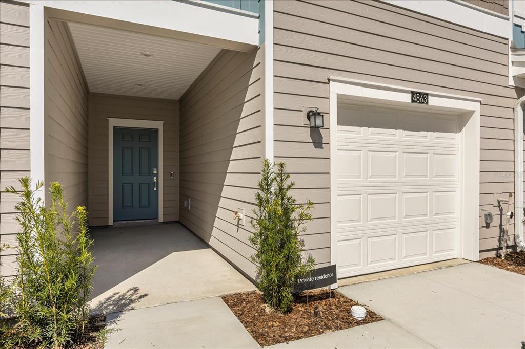 A tan-sided townhouse exterior features a blue front door, a white garage, and landscaping — 4863 SW 81ST LOOP, OCALA, FL