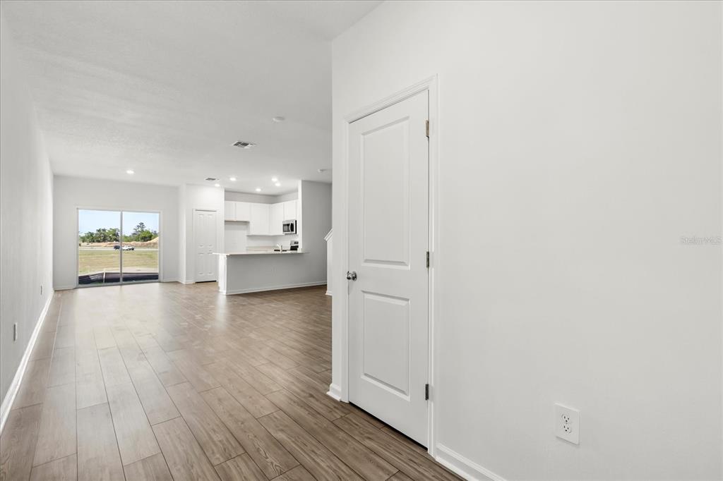 A bright, open-concept living area features light wood-look flooring, white walls, and a kitchen beyond — 4863 SW 81ST LOOP, OCALA, FL