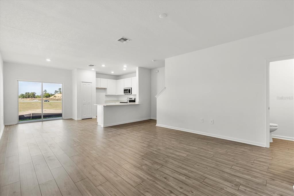 An open-concept living area with light wood-look flooring, a kitchen, and a sliding glass door — 4863 SW 81ST LOOP, OCALA, FL