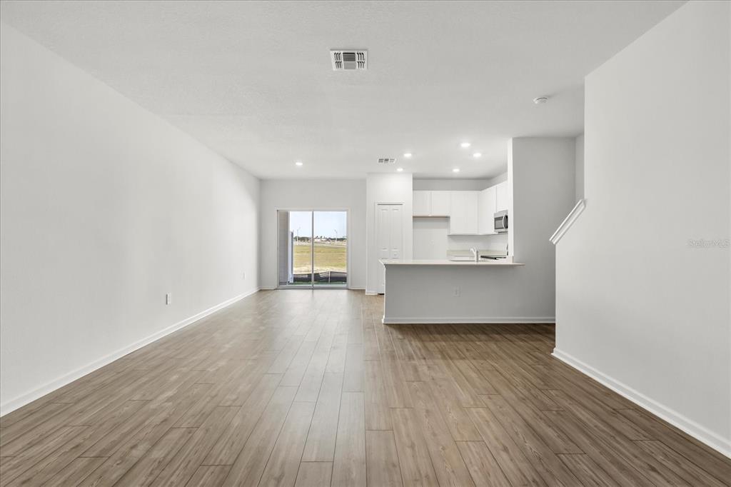 An open-concept living area with light wood-look flooring, a kitchen island, and sliding glass doors — 4863 SW 81ST LOOP, OCALA, FL