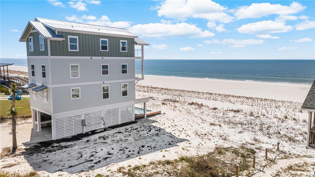 A three-story beach house with light siding stands on stilts next to the ocean — 1817 HIGHWAY 98, MEXICO BEACH, FL