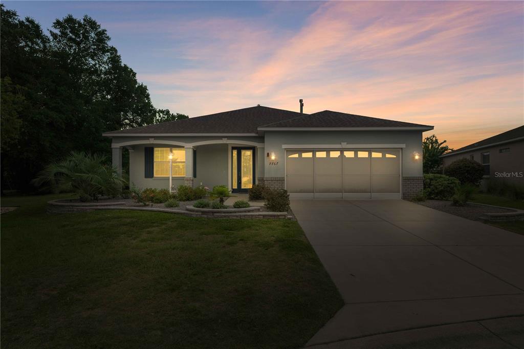 A single-story house with a garage and a landscaped front yard at sunset — 7767 SW 80TH PLACE ROAD, OCALA, FL