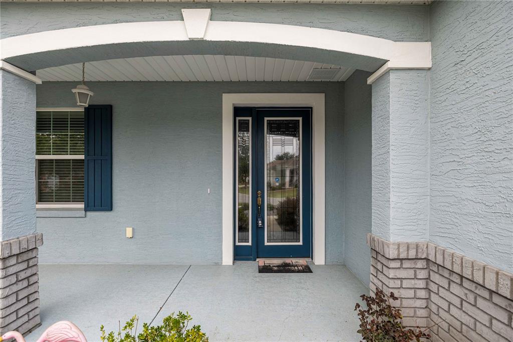 A covered front porch features a blue front door with glass panels and brick accents — 7767 SW 80TH PLACE ROAD, OCALA, FL
