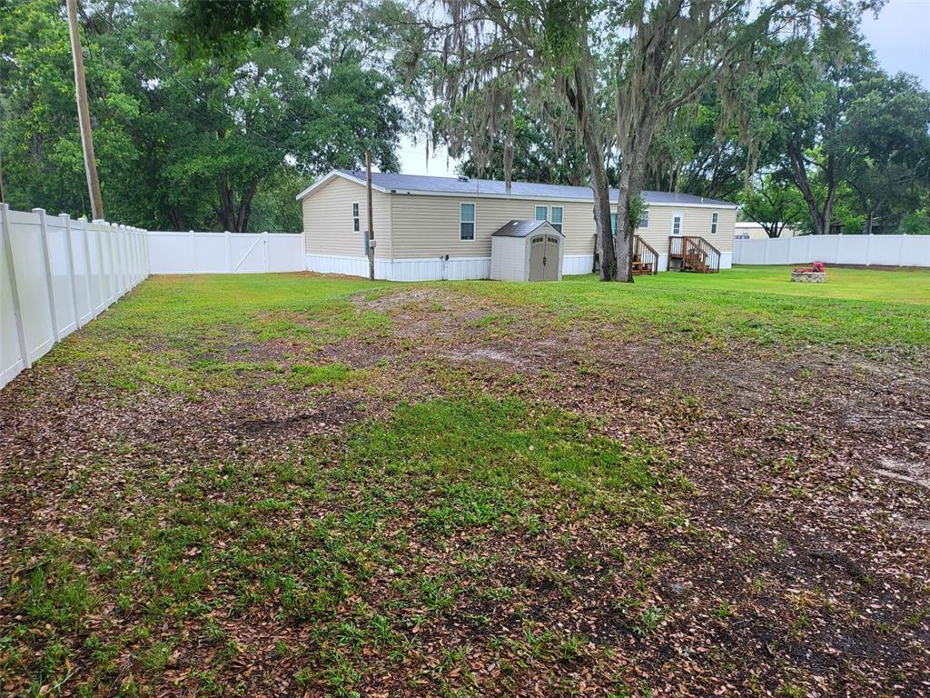 A beige manufactured home sits on a grassy lot enclosed by a white vinyl fence — 8915 HAMMOCK LOOP, POLK CITY, FL 33868, POLK CITY, FL