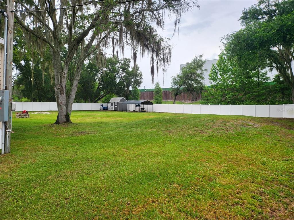 A large, grassy backyard features a storage shed, a metal carport, and a white fence — 8915 HAMMOCK LOOP, POLK CITY, FL 33868, POLK CITY, FL