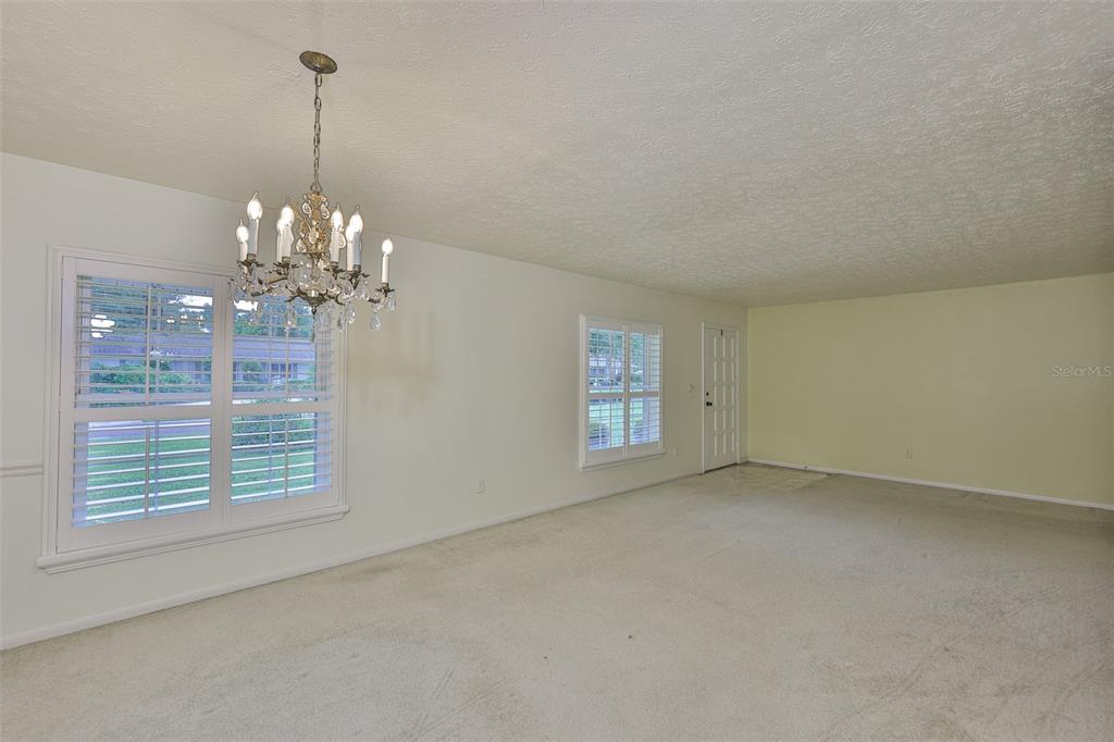 A carpeted dining room features a crystal chandelier, white plantation shutters, and light-colored walls — 1408 MOSS LADEN COURT, BRANDON, FL