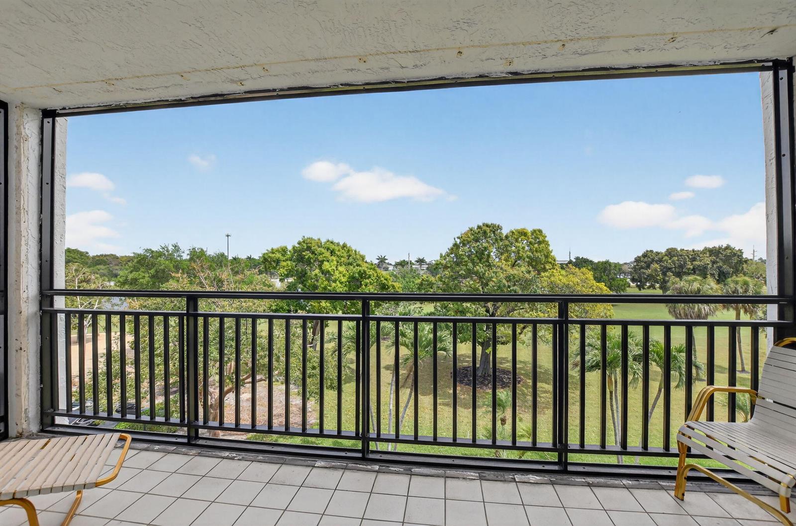 A balcony with white tile flooring, black metal railings, and two chairs overlooking a park — 7170 Promenade Drive # 401, Boca Raton FL 33433, BOCA RATON, FL