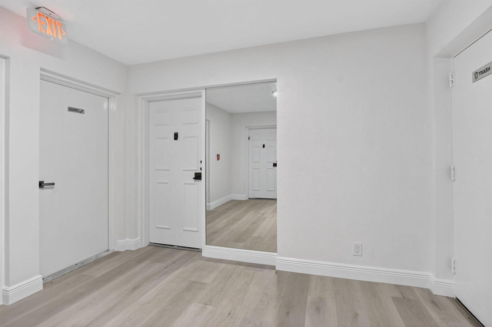 A hallway with light wood flooring, white walls, a mirrored wall, and several white doors — 7170 Promenade Drive # 401, Boca Raton FL 33433, BOCA RATON, FL