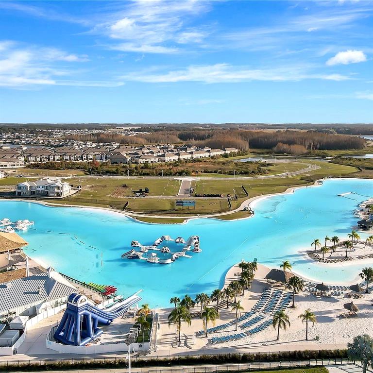 An aerial view shows a large turquoise lagoon with a water park and sandy beach — 7559 SWEETER TIDE TRAIL, WESLEY CHAPEL, FL
