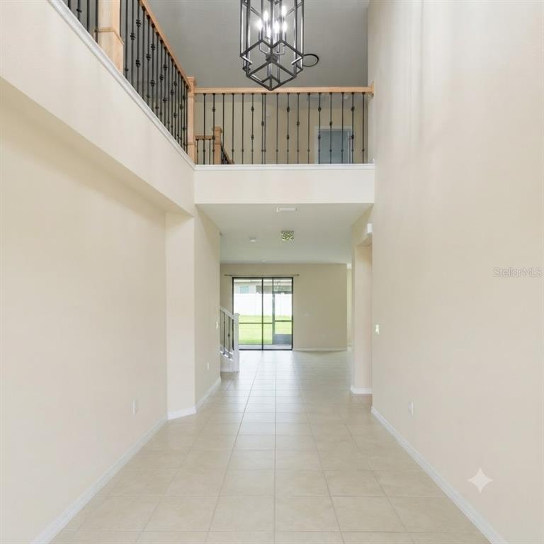 A two-story foyer features tile flooring, a metal chandelier, and a wooden staircase railing — 7559 SWEETER TIDE TRAIL, WESLEY CHAPEL, FL